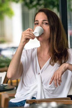 Dışarıda oturan bir fincan espresso kahve içen bir kadının portresi.