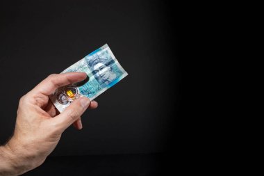Beş poundluk banknot tutan bir erkek el, siyah üzerinde izole edilmiş.