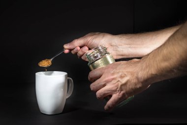 Siyah üzerinde izole beyaz bir kupa üzerinde granüle anında kahve dökme erkek el.