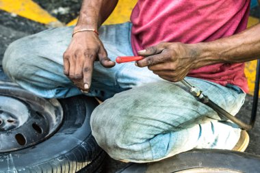 Galle, Sri Lanka'da bir benzin istasyonunda açık havada lastik üzerinde oturan bir lastik tamircisi.