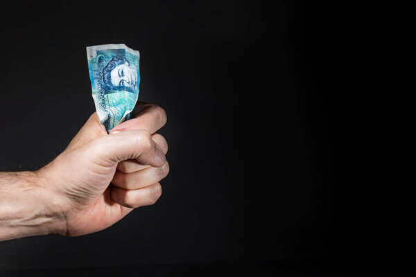 Мужская рука держит пятифунтовую банкноту на кулаке, изолированную над черным
.