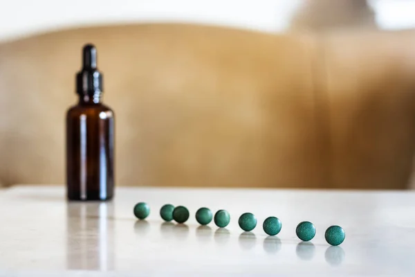 Spirulina pills in line on a table next to a brown bottle with dropper.