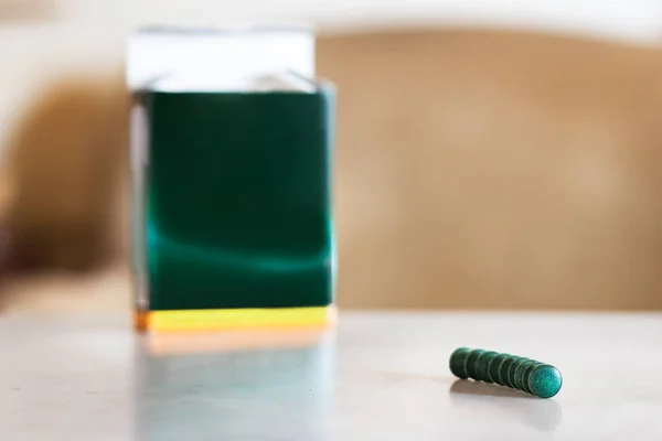 Spirulina pills in line on a table next to a box background.