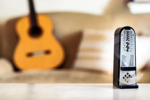 Mechanical metronome in motion, over a wooden classical acoustic guitar background.