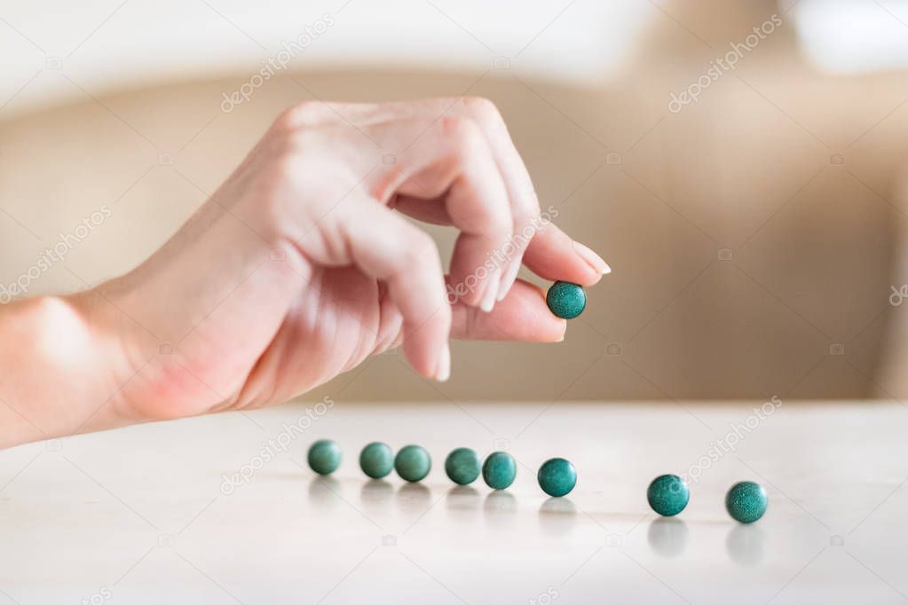 Female hand holding a spirulina pill next to pills on a table.