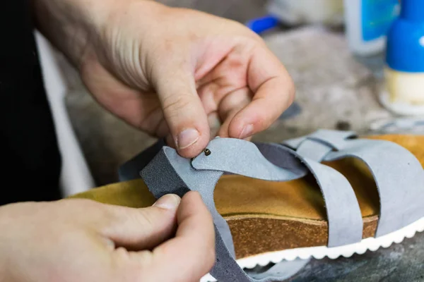 Male shoemaker hands repairing a leather sandal.