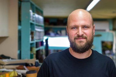 Sakallı kel bir mand Portresi, ayakkabıcı onun atölyesinde kamera görünümlü, yumuşak gülümseme.