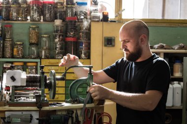 Atölyesinde eski bir perçin pres makinesi işleten bir erkek ayakkabıcı.