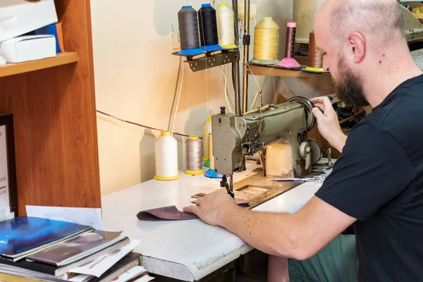 A male shoemaker sewing leather with an old sewing machine.