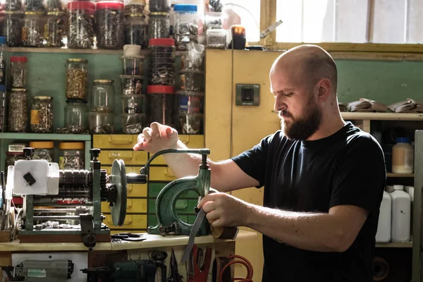 Atölyesinde eski bir perçin pres makinesi işleten bir erkek ayakkabıcı.