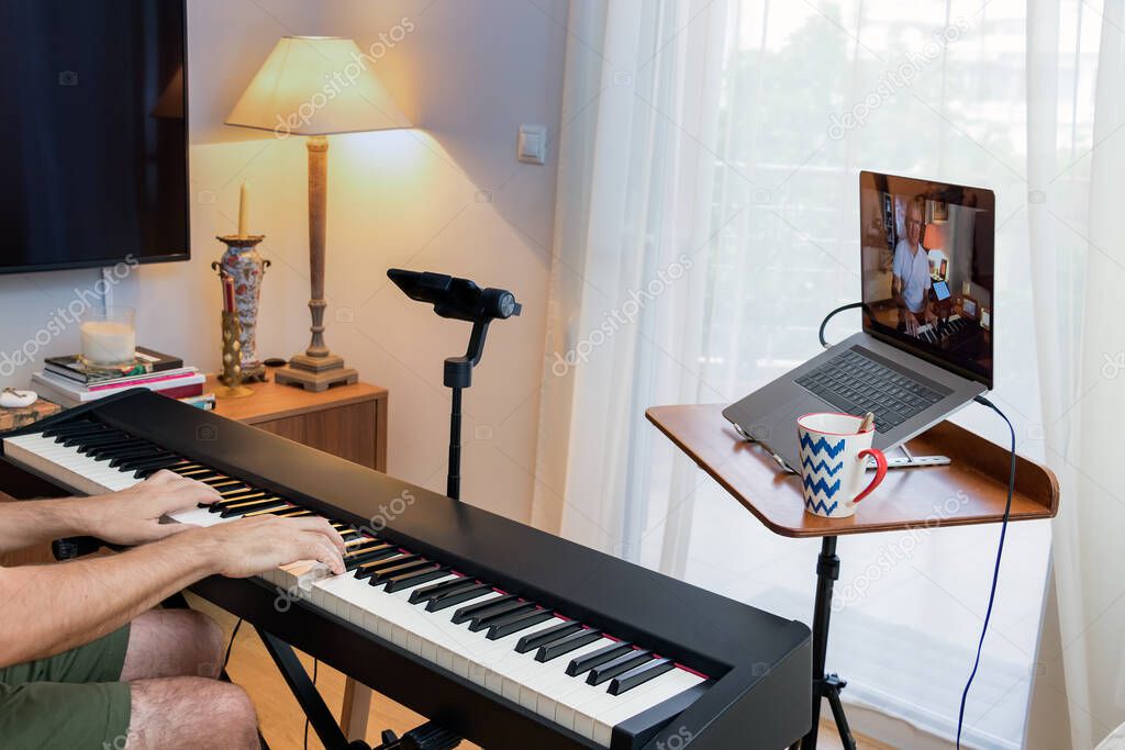 Male piano teacher giving piano lessons online at home using a laptop and a smarphone a smartphone as second camera.