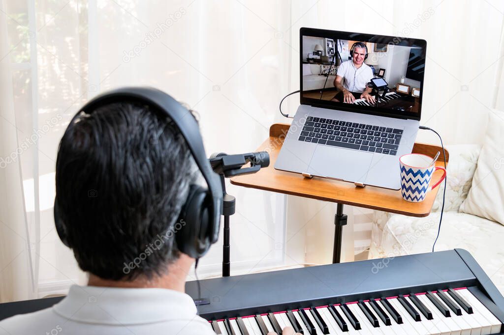 Male piano teacher giving piano lessons online at home using a laptop.
