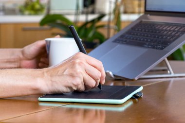 Evde çalışırken grafik tableti ve dizüstü bilgisayar kullanan kadın tasarımcı elleri