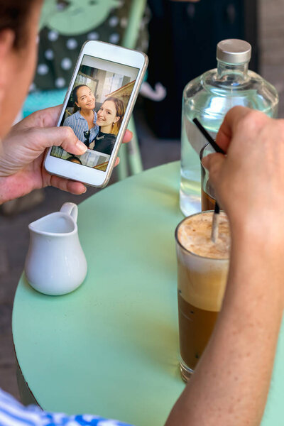 Female hand holding a mobile phone while having coffee looking photos.