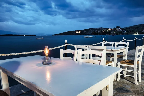 Ξύλινα παραδοσιακά τραπέζια και καρέκλες ελληνικής ταβέρνας τη νύχτα και θέα στην παραλία της Αμαλιάπολης — Φωτογραφία Αρχείου