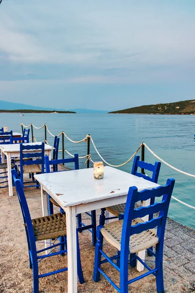 Mesas tradicionales de madera blanca y sillas de una taberna griega por la noche y la vista de la playa de Amaliapoli, Grecia Imagen de archivo