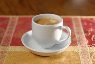 Bir fincan espresso kahve, kırmızı ve altın kaplama bir masa üzerinde.