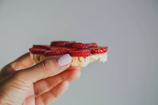 Crispbread with strawberries in hand on a gray background
