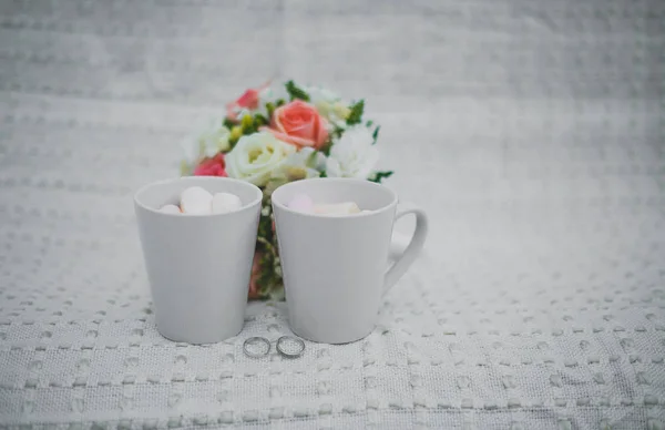 wedding photography. wedding details winter wedding. two white cups with and marshmallows, a bridal bouquet and rings