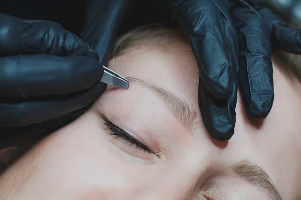 black beautician plucking eyebrows