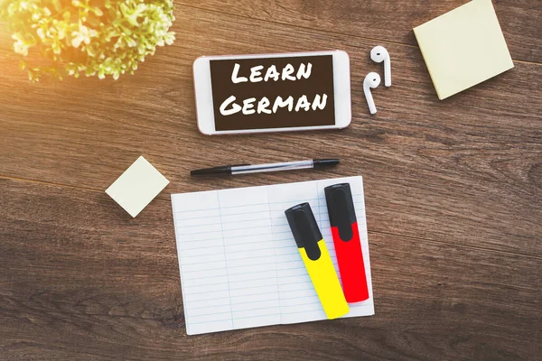 learn german inscription, smartphone, wireless headphones, notepad, concept of learning a foreign language