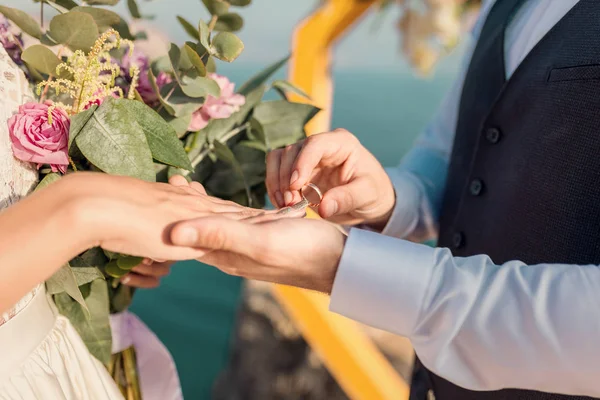 O noivo veste o anel para a ponte em uma cerimônia de casamento em uma praia do mar. Mãos recém-casadas, close-up — Fotografia de Stock