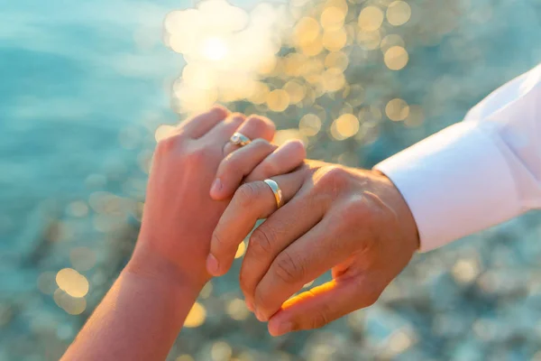 Düğün çift deniz günbatımı arka plan üzerinde el ele tutuşuyor