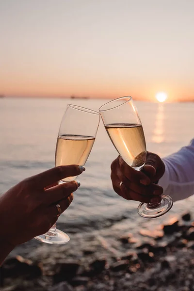 Kadın ve erkek, günbatımında şampanyayla şarap kadehlerini tıngırdatıyor.