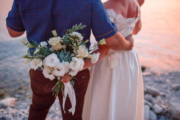 Svatební pár objímání, nevěsta drží kytici květin v ruce, ženich ji objímají — Stock fotografie