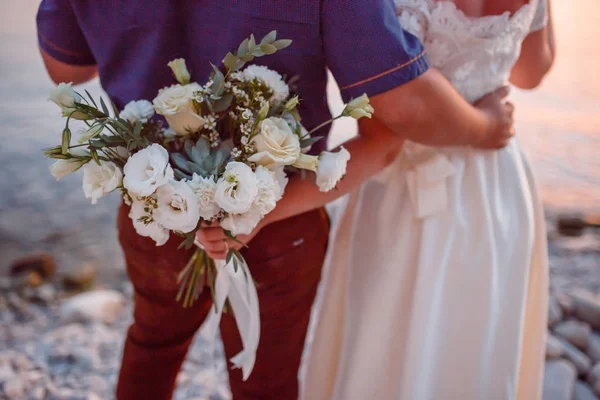 結婚式のカップルを抱いて、花の花束を保持して彼女の手に、彼女を抱きしめている新郎新婦 — ストック写真
