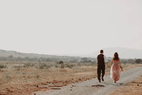 Gelin ve damat el ele tutuşup gelinliklerle koşuyorlar. Gelin elinde bir buket çiçek tutuyor.