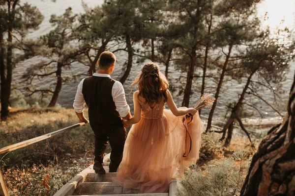 Gelin ve damat el ele tutuşup kumsalda koşuyorlar. Gelin elinde bir buket çiçek tutuyor.