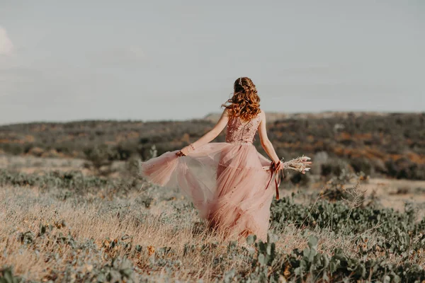 Şık gelin elinde düğün buketiyle gün batımında dağların güzel manzarasında dikiliyor.