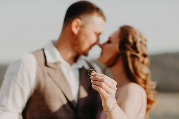 Kissing newlyweds take their wedding rings on the the mountain background — Stock Photo, Image