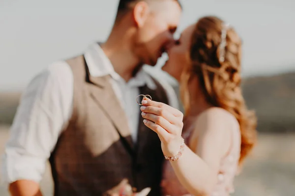 Kissing newlyweds take their wedding rings on the the mountain background — Stock Photo, Image