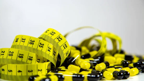 Pills with measuring tape on white background, represent the diet pill industry — Stock Photo, Image