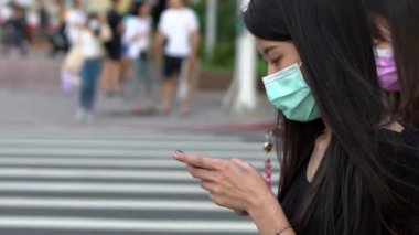 Taipei, Tayvan-04 Haziran 2020: Sokakta koronavirüs enfeksiyonunu önlemek için Asyalı kadın yüz maskesi takıyor. Sosyal ağlarda mesajlaşmak için modern akıllı telefonu kullanmak. Yaşam tarzı konsepti. - Dan.