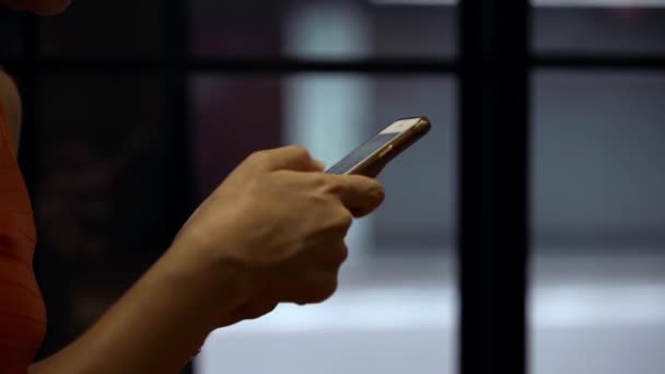 在一个有窗户背景的棺材里 把拿着智能手机的亚洲女人的手关上 在喝咖啡休息的时候 女孩在手机上观看和发短信 — 图库视频影像