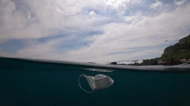 İnsanlar okyanus suyuna tıbbi bir maske fırlatıyor. Denizin altında yüzen cerrahi maskeler kullanılmış. İşe yaramaz koronavirüs hijyenik maskesi. Bulaşıcı atık Dan
