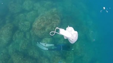 Tıbbi yüz maskesi suyun altında yüzüyor. Kullanılmış cerrahi maskeleri okyanus suyuna uygun olmayan bir şekilde atmak. Koronavirüs Covid-19 'un korunması için tek kullanımlık yüz maskesi.