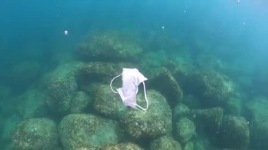 Koruyucu maske atıldı ve okyanusa atıldı. Terk edilmiş yüz maskesi denizin altında yüzüyor. Coronavirus Covid-19 'u korumak için cerrahi maskeler kullanılmış.