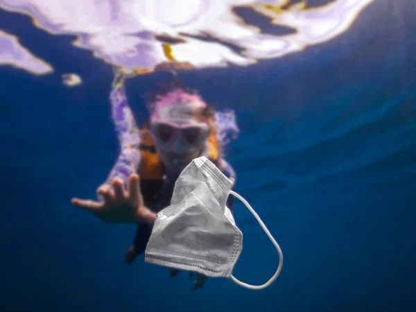 ボランティアの女性スキューバダイバーは水中を探検し 海をきれいにしています 使い捨てマスクをキャッチ青い水にゴミを発生させます 海の健康を脅かす海岸のゴミ — ストック写真