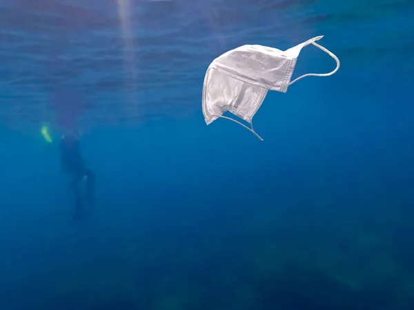 スキューバダイバーは水中を探検し 海をきれいにしています 使い捨てマスクをキャッチ青い水にゴミを発生させます 海の健康を脅かす海岸のゴミ — ストック写真