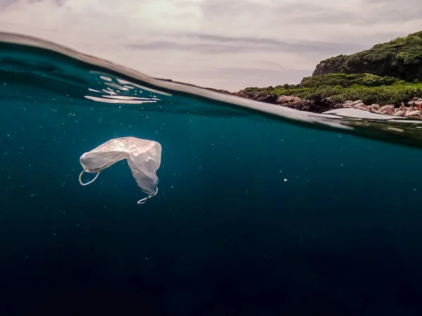 海に捨てられた保護マスク 放棄されたマスクは海の水中に浮かんでいます コロナウイルスを保護するために使用される外科用マスク Covid — ストック写真