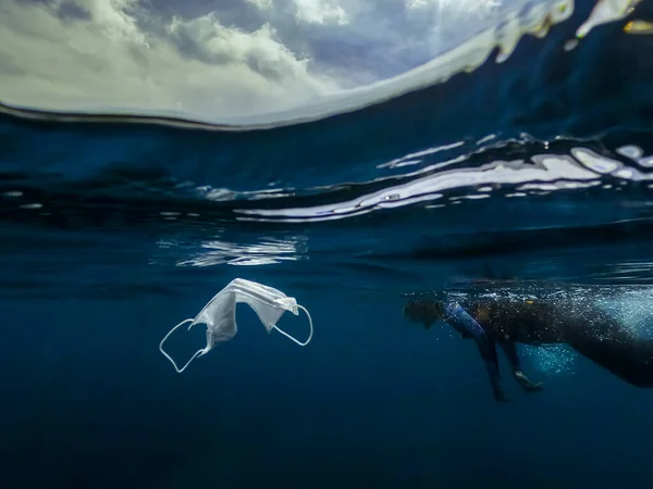 Waste during COVID-19. Volunteer woman snorkeler diving underwater and cleaning up the ocean. The volunteer catch a single-use face masks garbage from the water. Coronavirus concept.