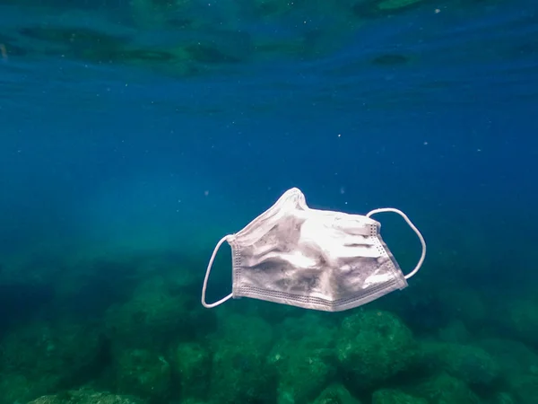 海に捨てられた保護マスク 放棄されたマスクは海の水中に浮かんでいます コロナウイルスを保護するために使用される外科用マスク Covid — ストック写真