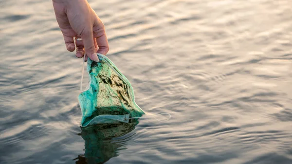 使い捨て医療用のマスクを捨て海に浮かぶ女性の手を拾う コロナウイルスプラスチック廃棄物環境汚染 海の健康を脅かす海岸のゴミ — ストック写真