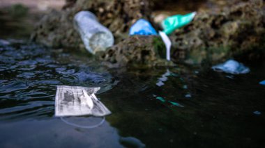 Tıbbi atık, maskeler, plastik şişe ve eldivenler deniz suyundaki çöpler. Coronavirus covid-19 çevre kirliliği hastalığı. Plaja atılan cerrahi maske kullanılmış..