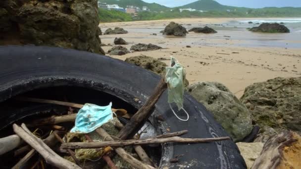 海上医療廃棄物 マスクやプラスチック手袋ゴミゴミ コロナウイルスCovid 19汚染疾患環境 ビーチの海岸に投げ青の外科用マスクを使用しました — ストック動画