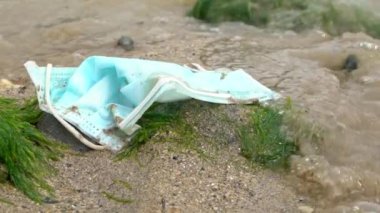 Tıbbi atıklarla dolu keşiş yengecinin yavaşlaması deniz suyundaki çöpleri maskeliyor. Coronavirus covid-19 çevre kirliliği hastalığı. Bir sahilin kıyısına atılmış ameliyat maskesi. -Dan.